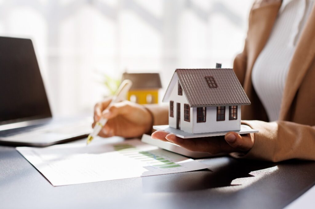 Female woman hand holding home model, investment small miniature white toy house. Mortgage property insurance dream moving home and real estate concept